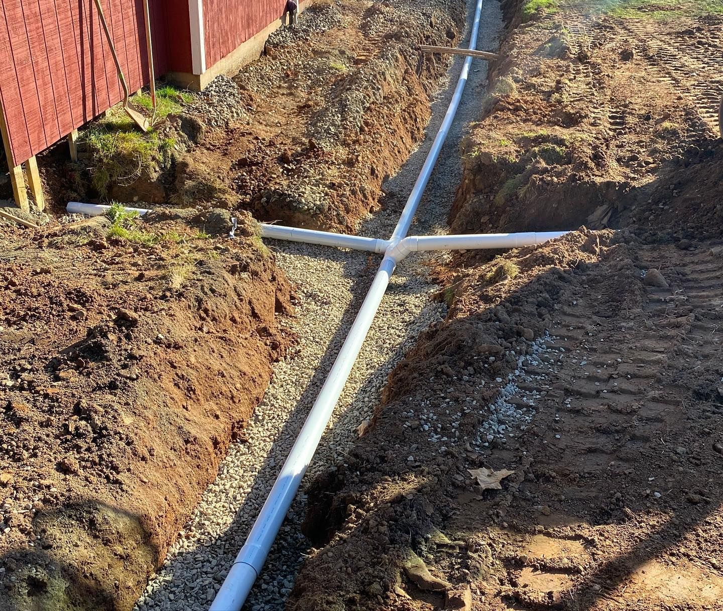 A trench with white drainage pipes installed, surrounded by gravel and dirt.