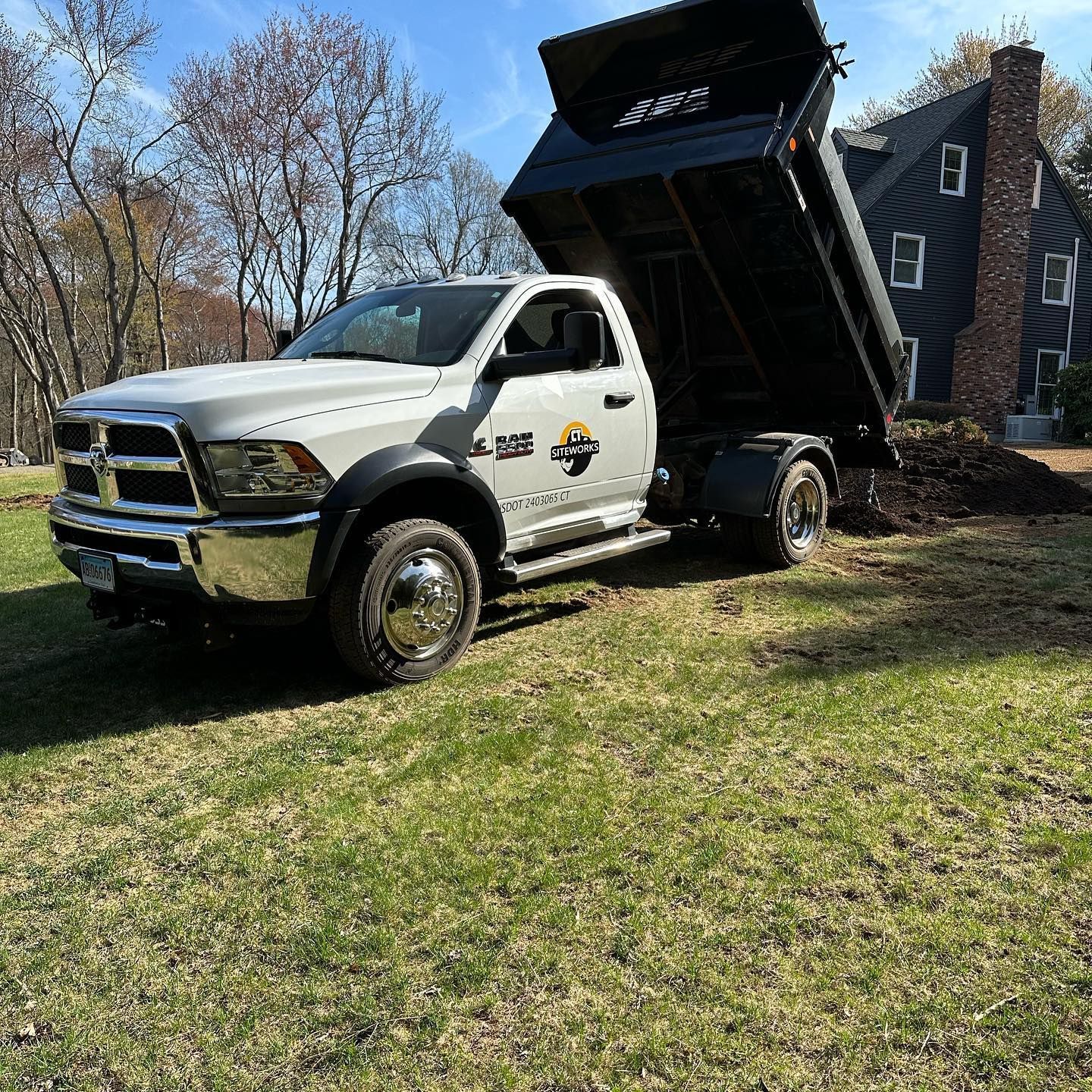 White dump truck on grass in front of a house, bed tilted up.