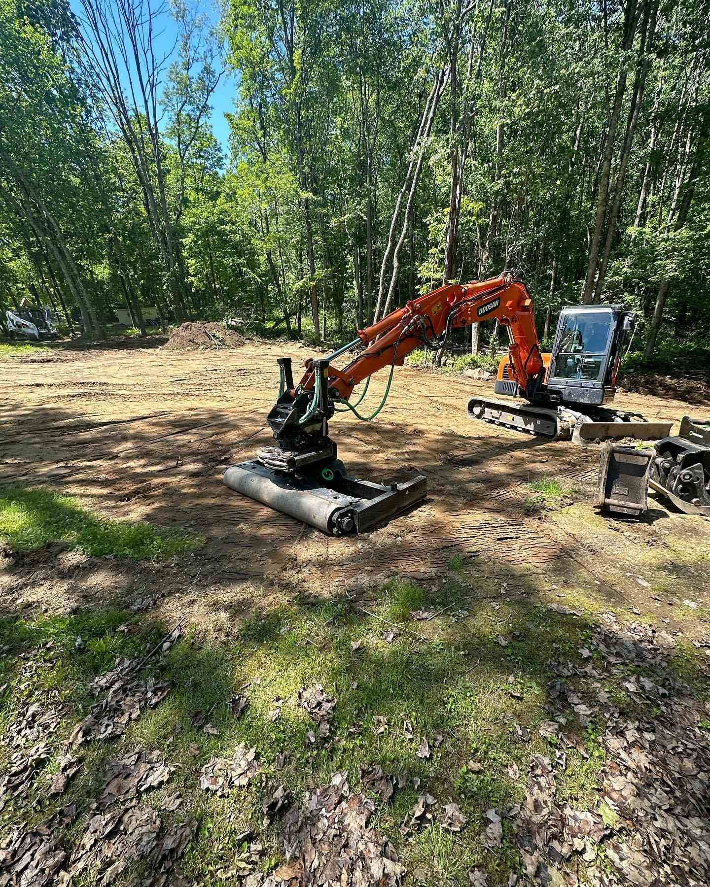 Orange excavator on cleared land surrounded by trees.