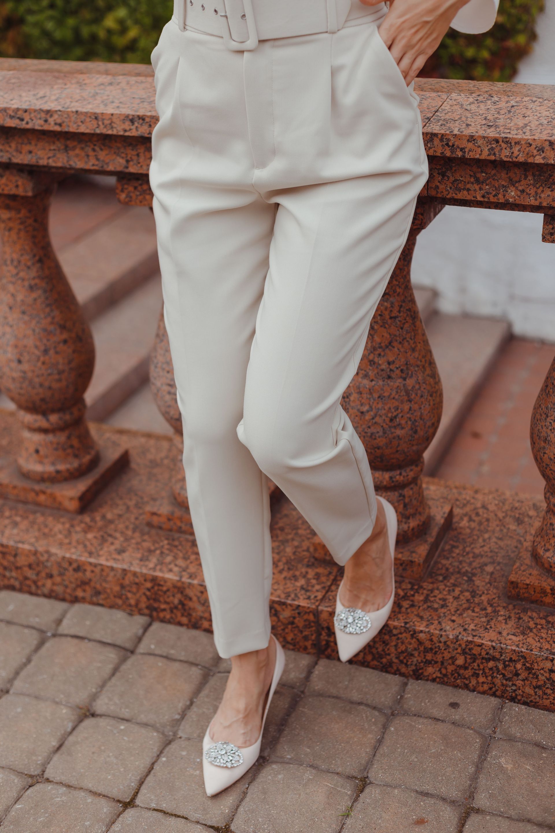 Persona vestida con pantalones y blusa color crema, de pie junto a una barandilla de piedra, con zapatos planos estampados.