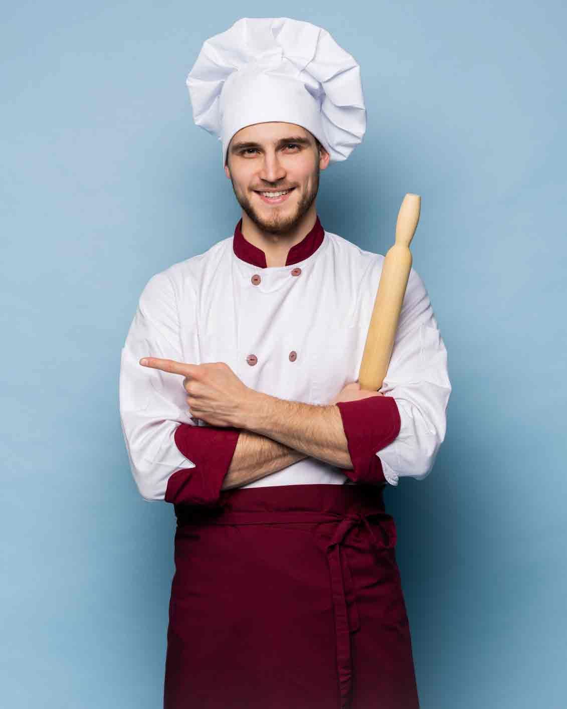 A chef is holding a rolling pin and pointing at the camera.