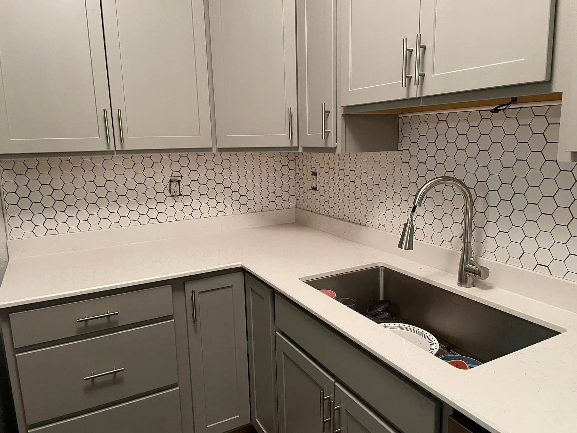 A kitchen with gray cabinets and a stainless steel sink