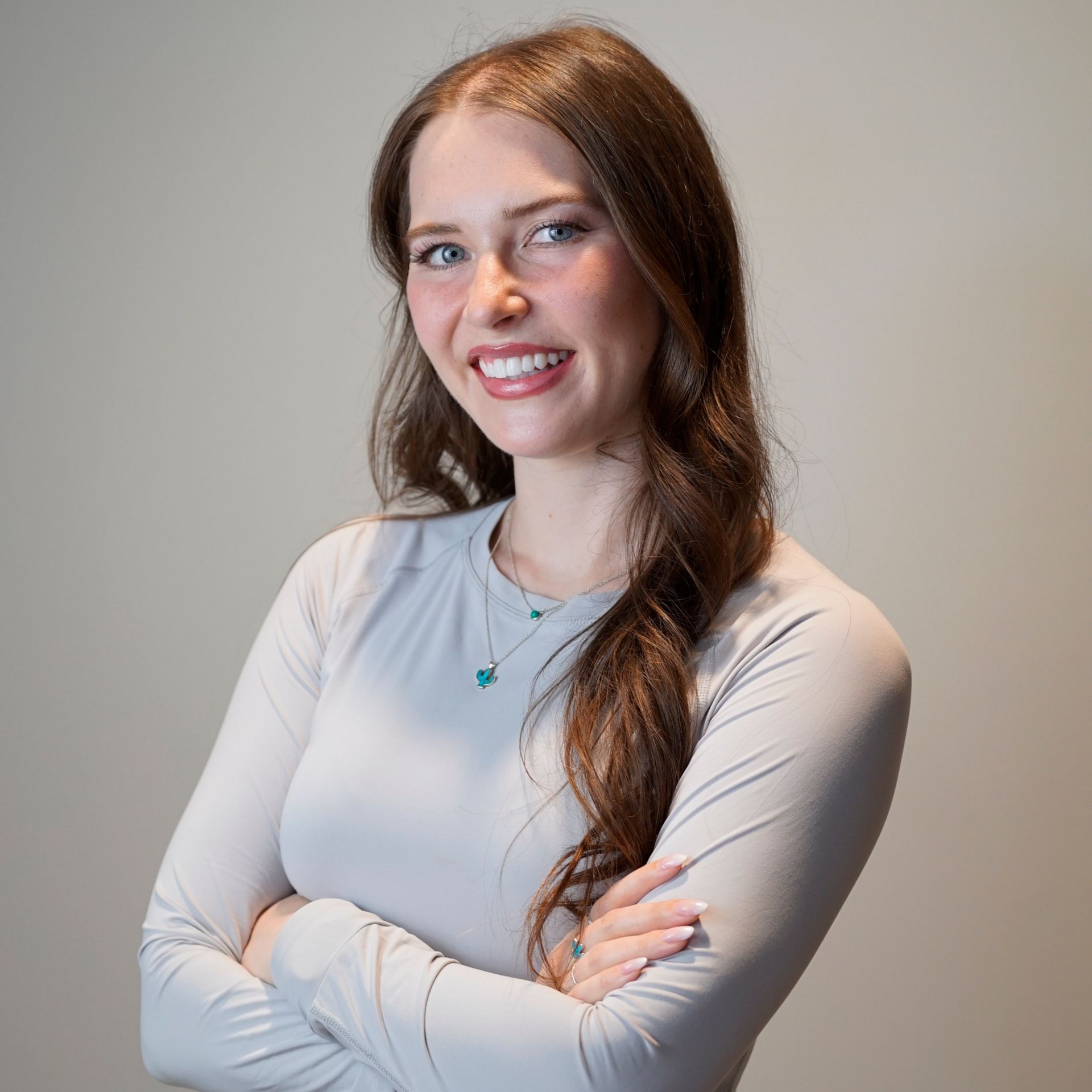 Woman with brown hair smiles at the camera. She wears a black shirt, indoors, with light-colored background.