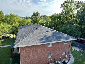 An aerial view of a brick house with a new roof surrounded by trees.