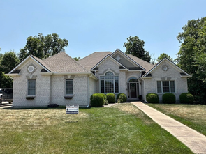 A large white brick house with a sign in front of it.