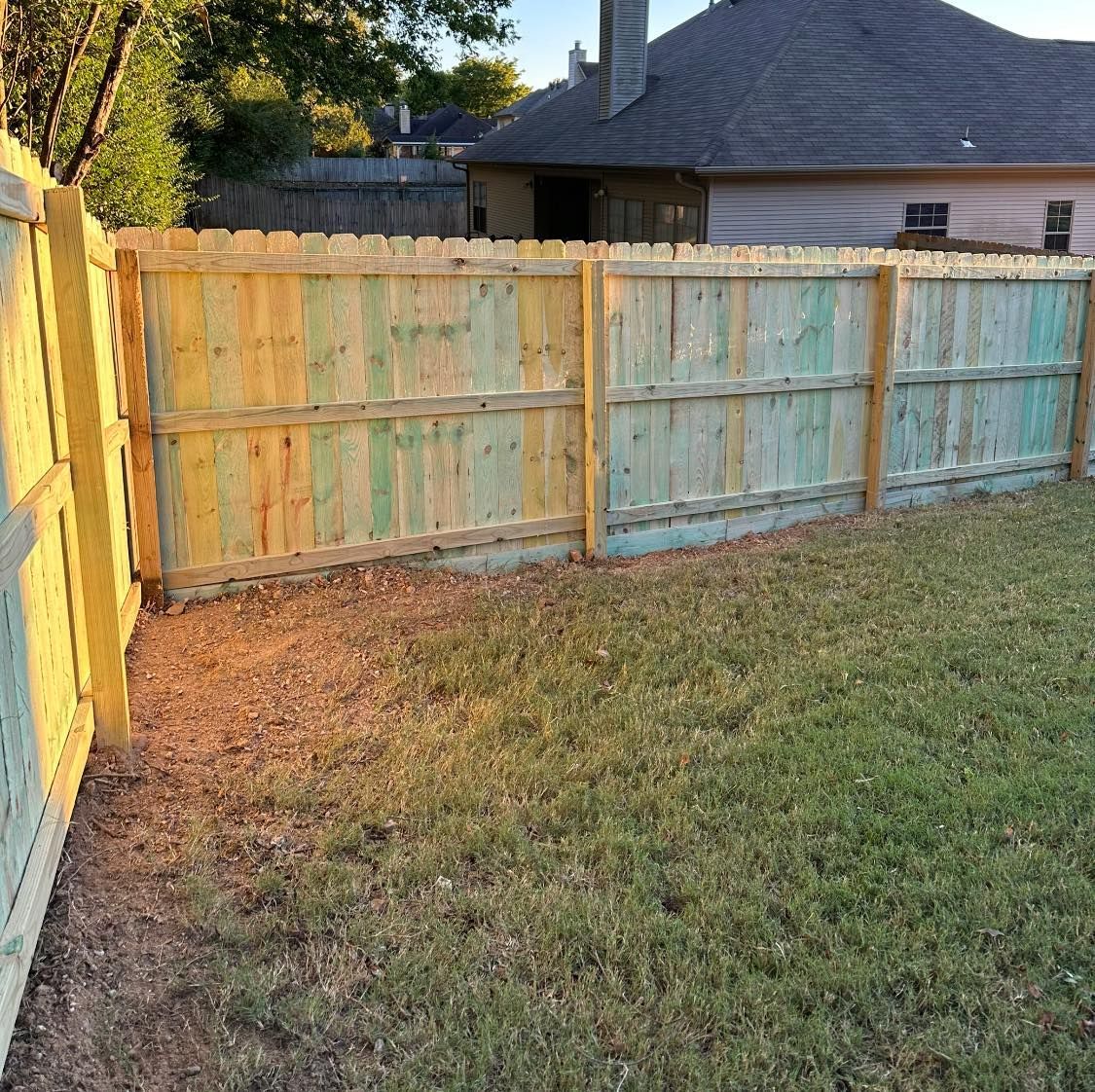 A wooden fence in a backyard with a house in the background.
