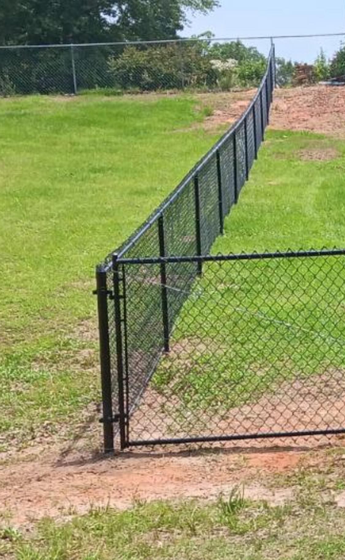 A chain link fence is surrounding a grassy field with a gate.