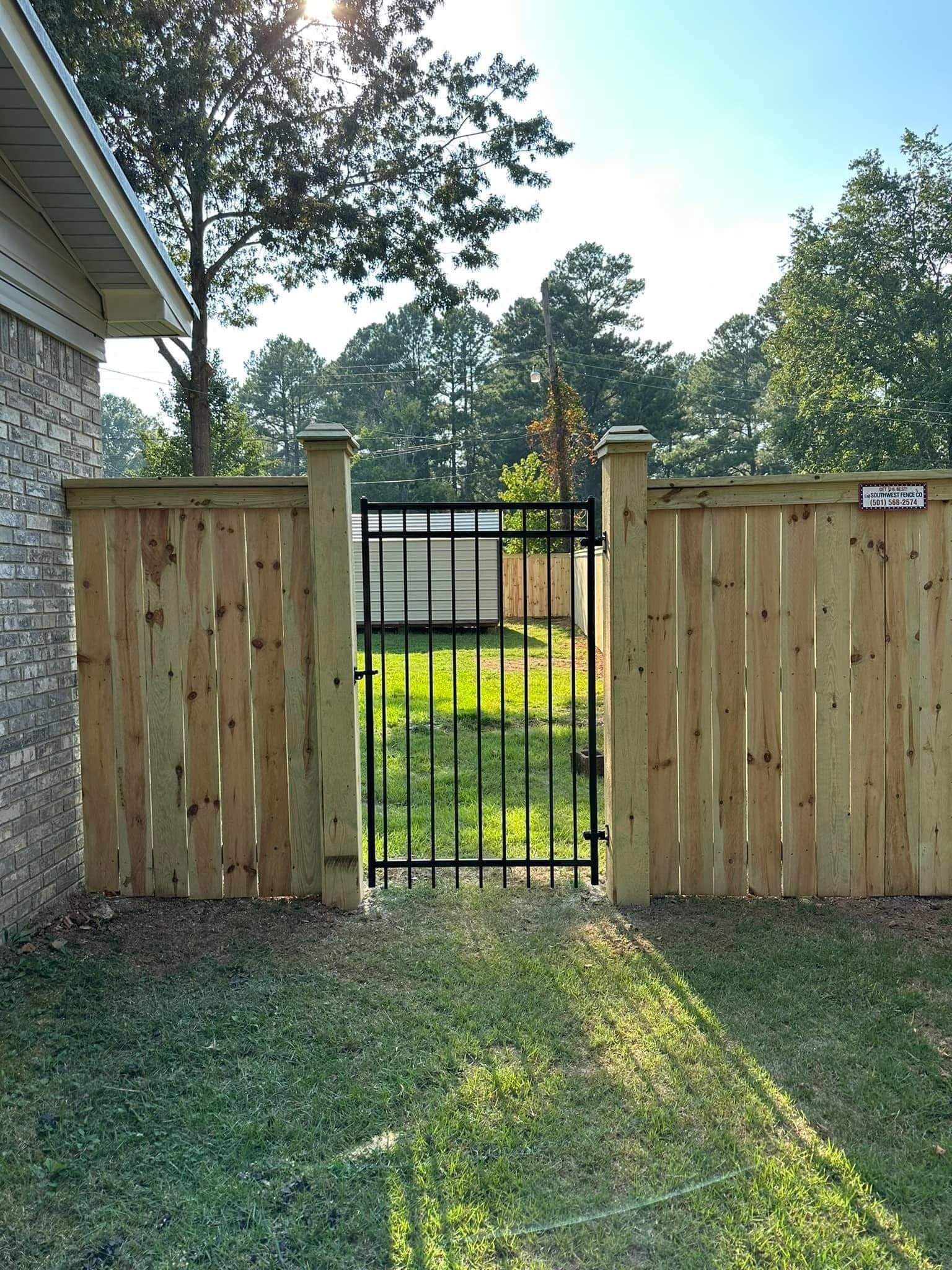 A wooden fence with a metal gate leading to a yard.