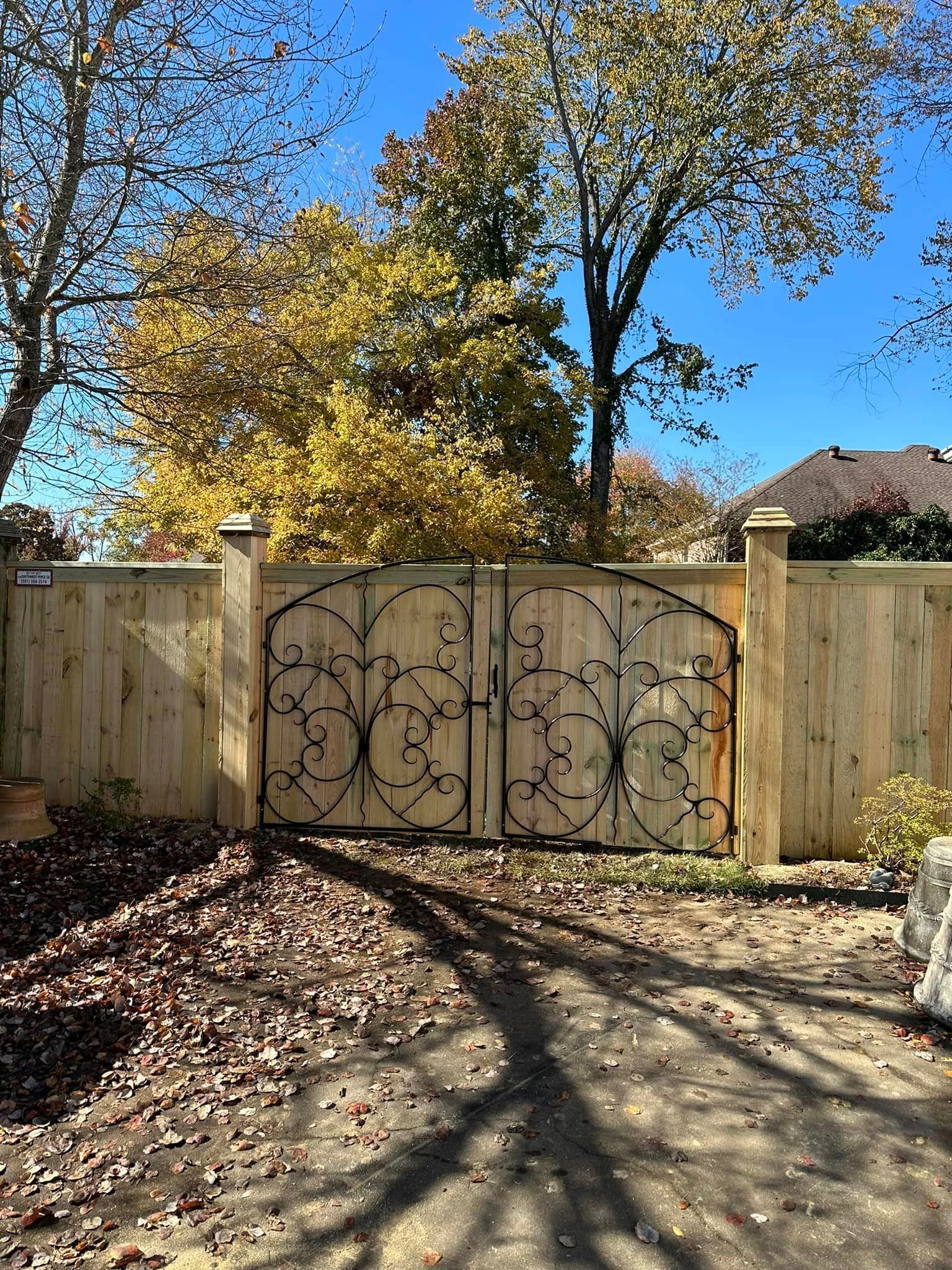 A wooden fence with a wrought iron gate in front of it.