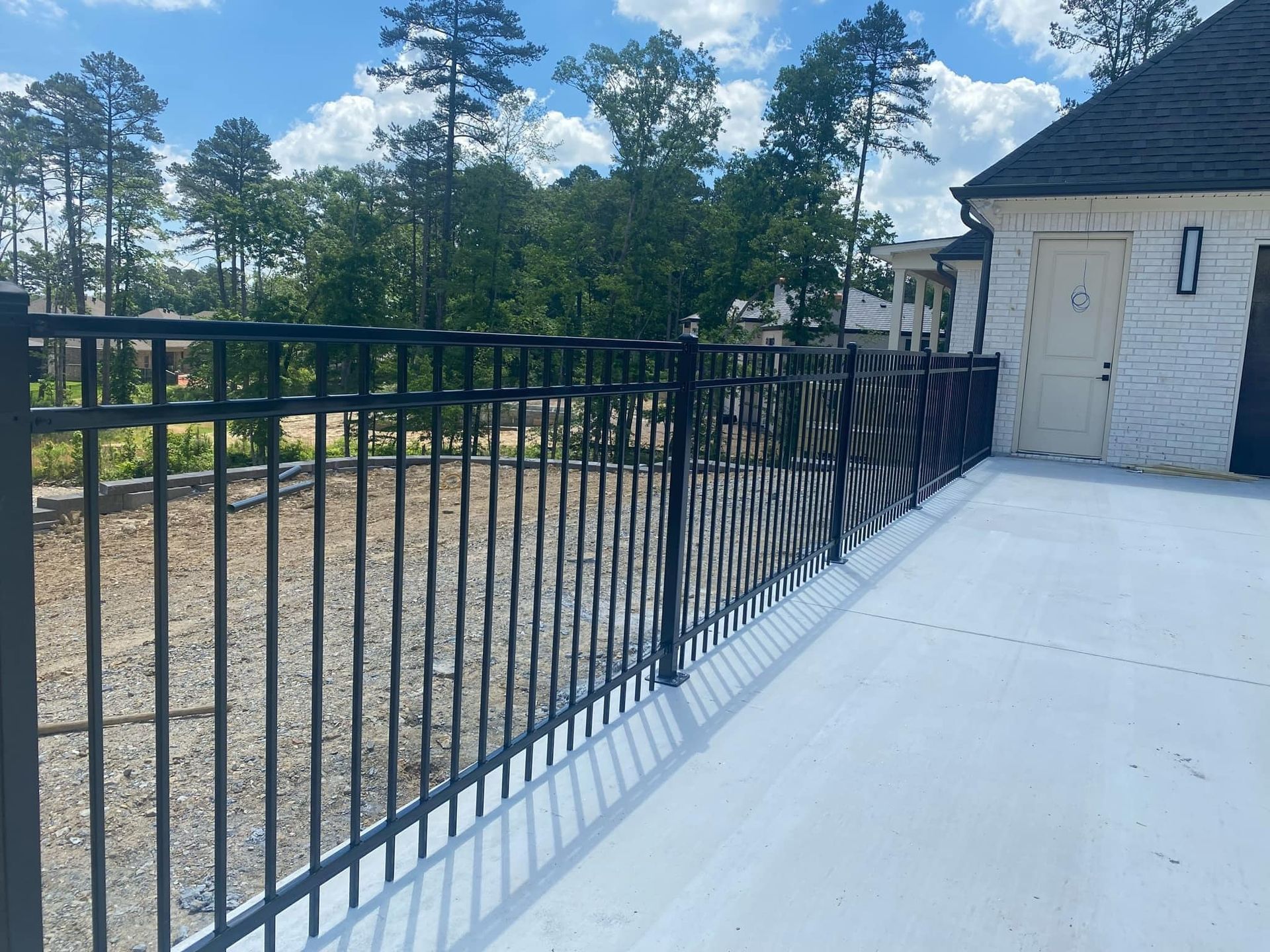 A black fence surrounds a white brick building with trees in the background.