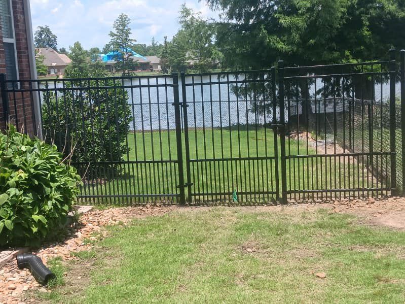A black metal fence surrounds a lush green yard with a lake in the background.