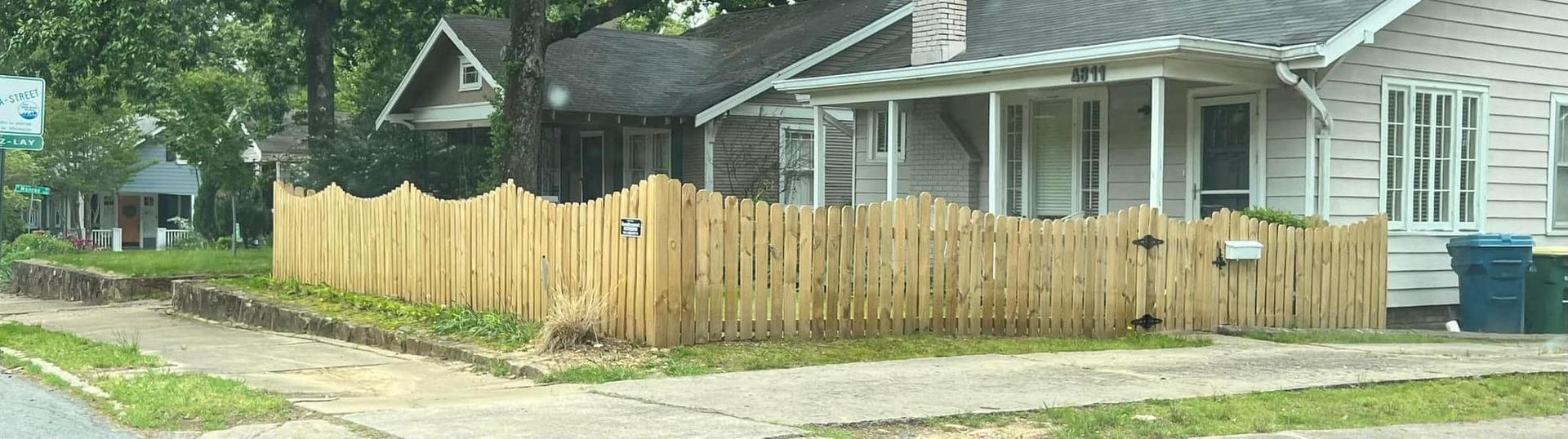 A wooden fence is surrounding a house on the side of the road.