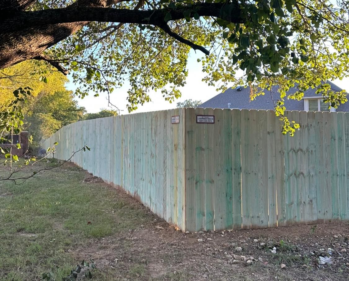 A wooden fence is surrounded by grass and trees in front of a house.