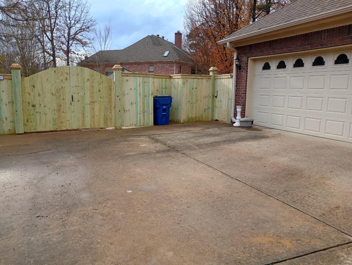 A wooden fence surrounds a driveway next to a garage.