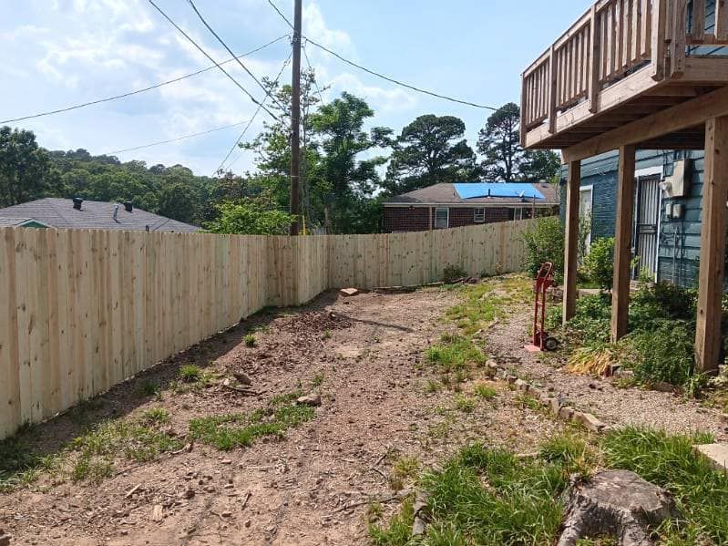 A wooden fence surrounds a dirt road in front of a house.
