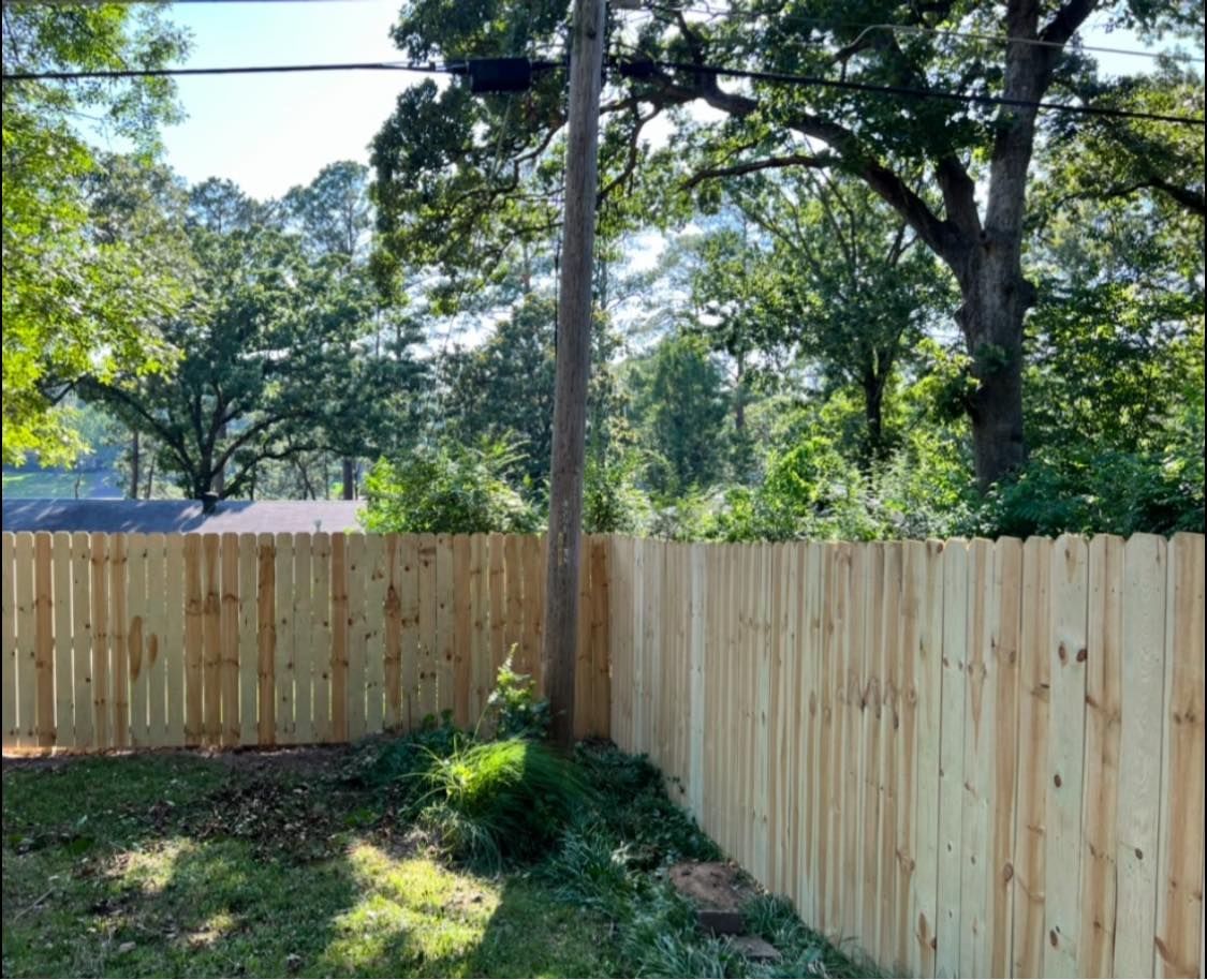 A wooden fence is surrounded by trees and a power line in Little Rock