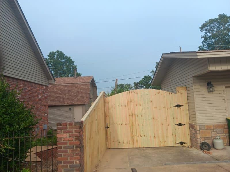 A wooden fence surrounds a driveway leading to a house