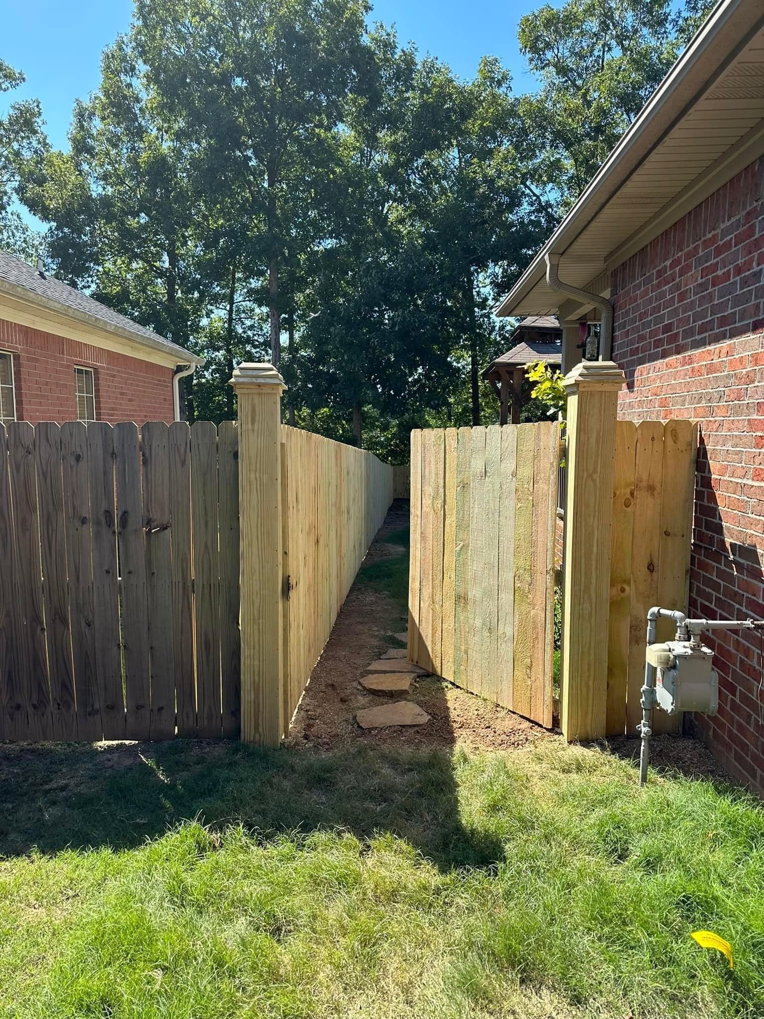 A wooden fence with a gate leading to a brick house.