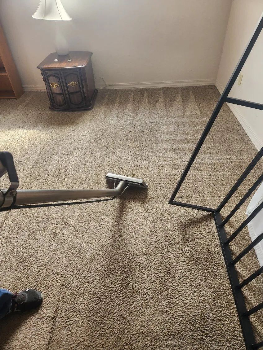 Carpet being professionally cleaned with a vacuum. Beige carpet, furniture, and metal railing in a room.