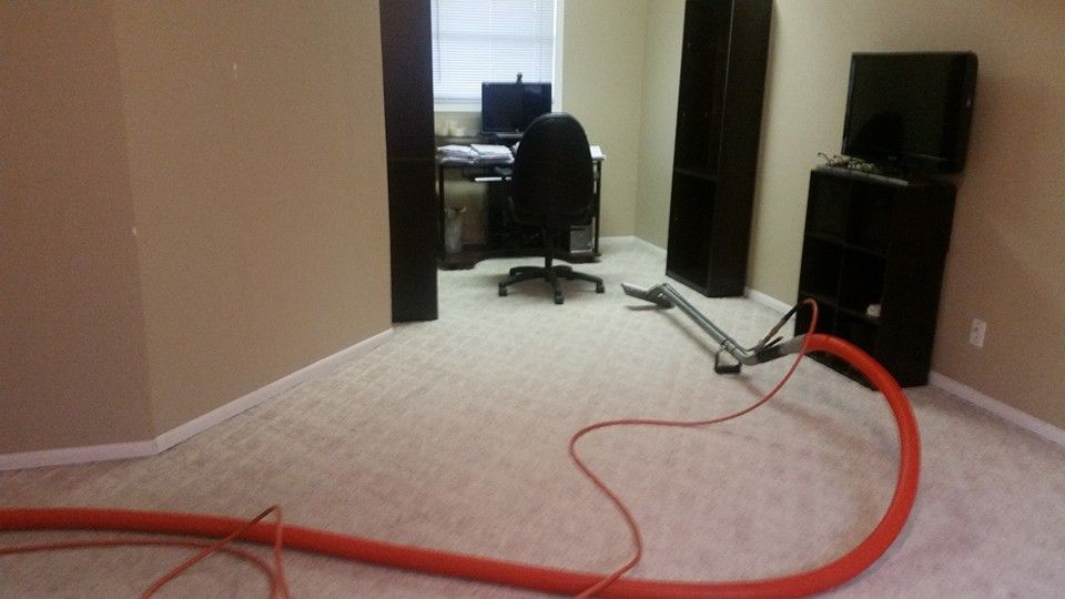 A room with a desk and chair and a vacuum on the floor