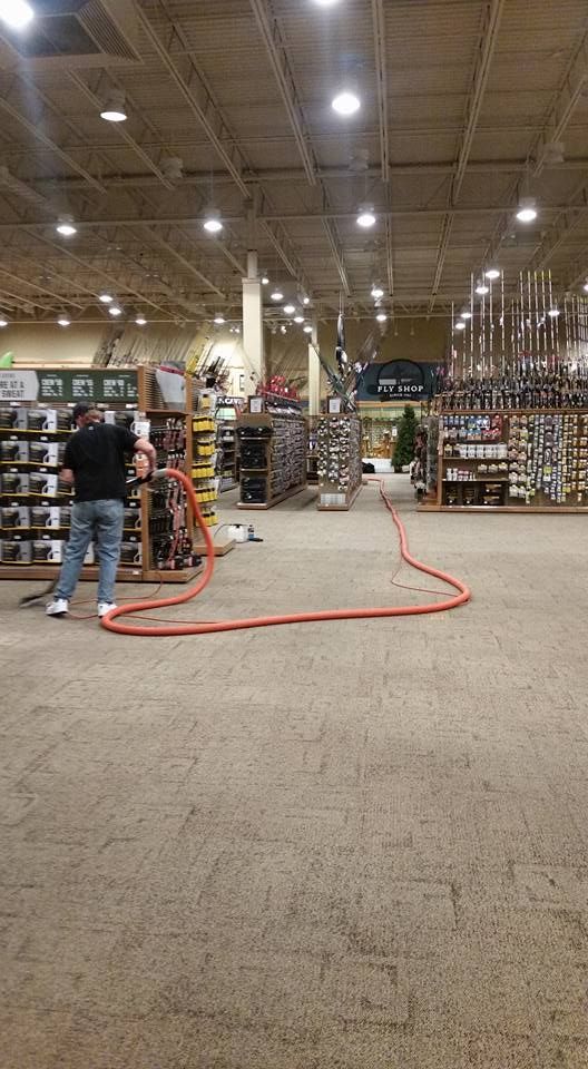 A man is cleaning the floor of a store with a hose.