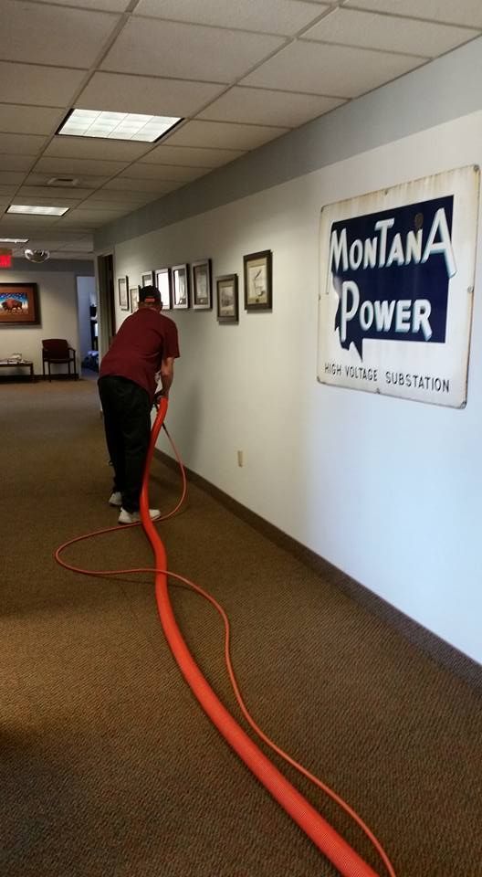 A man is vacuuming a hallway with a montana power sign on the wall.