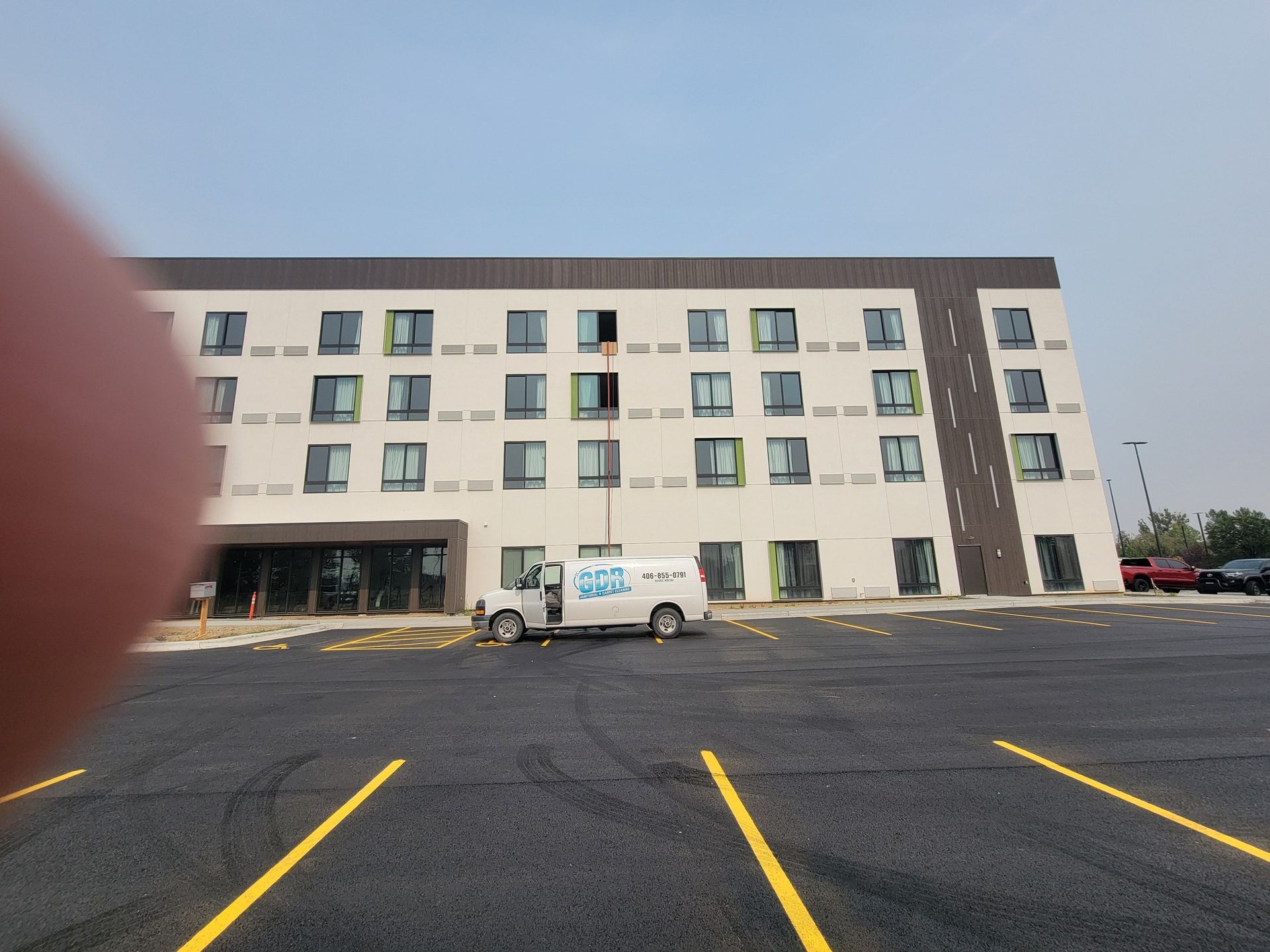 A white van is parked in front of a large building in a parking lot.