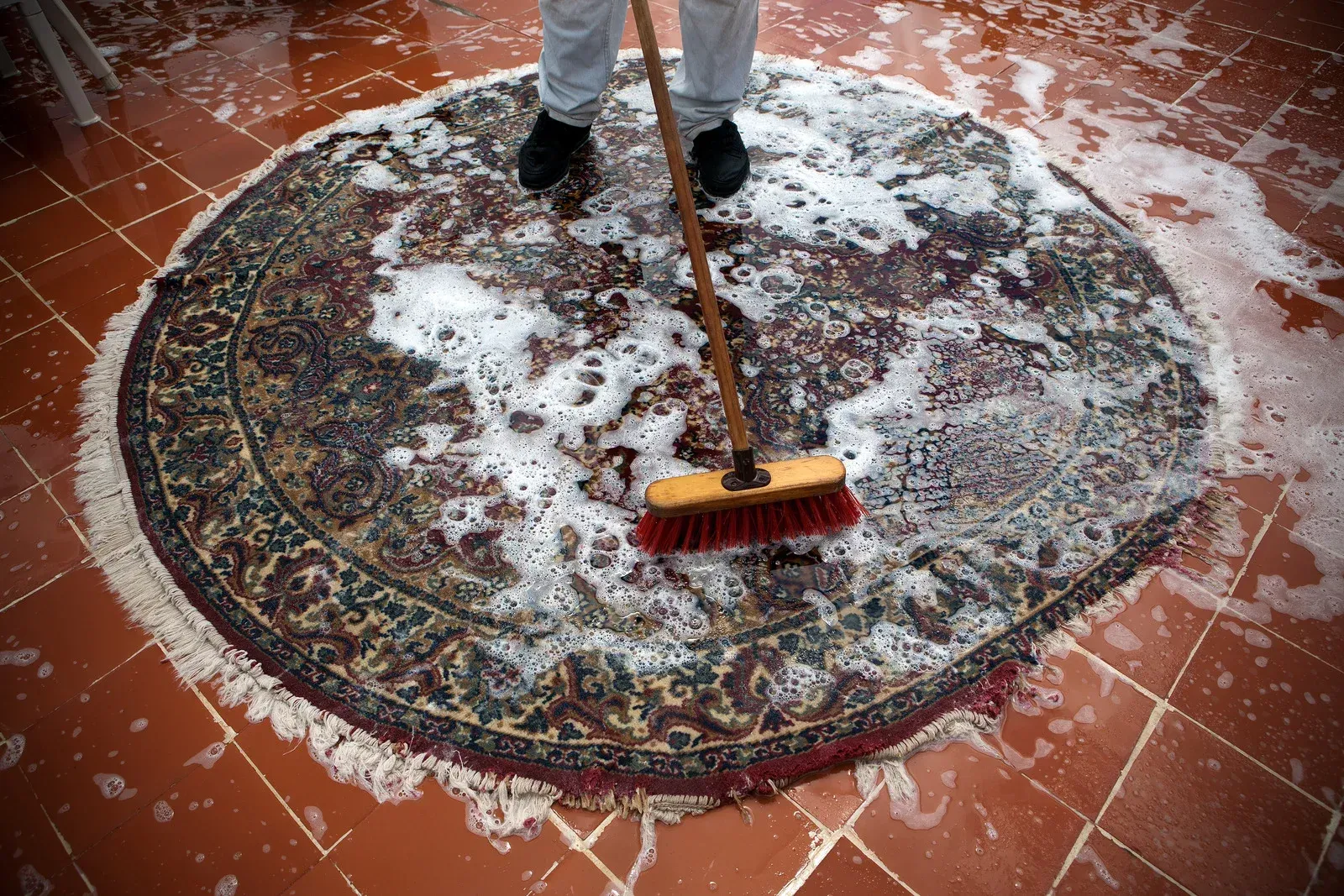 A person is cleaning a rug with a broom.
