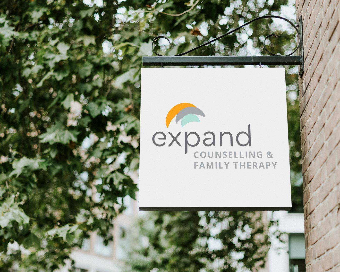 A sign for expand counseling and family therapy hangs from a tree