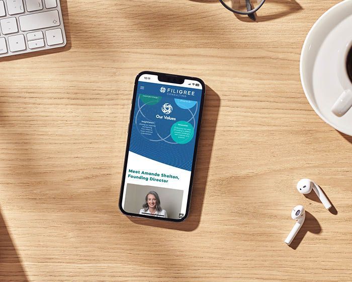 A cell phone is sitting on a wooden table next to a keyboard and headphones.