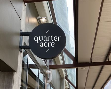 A sign for quarter acre hangs from the side of a building