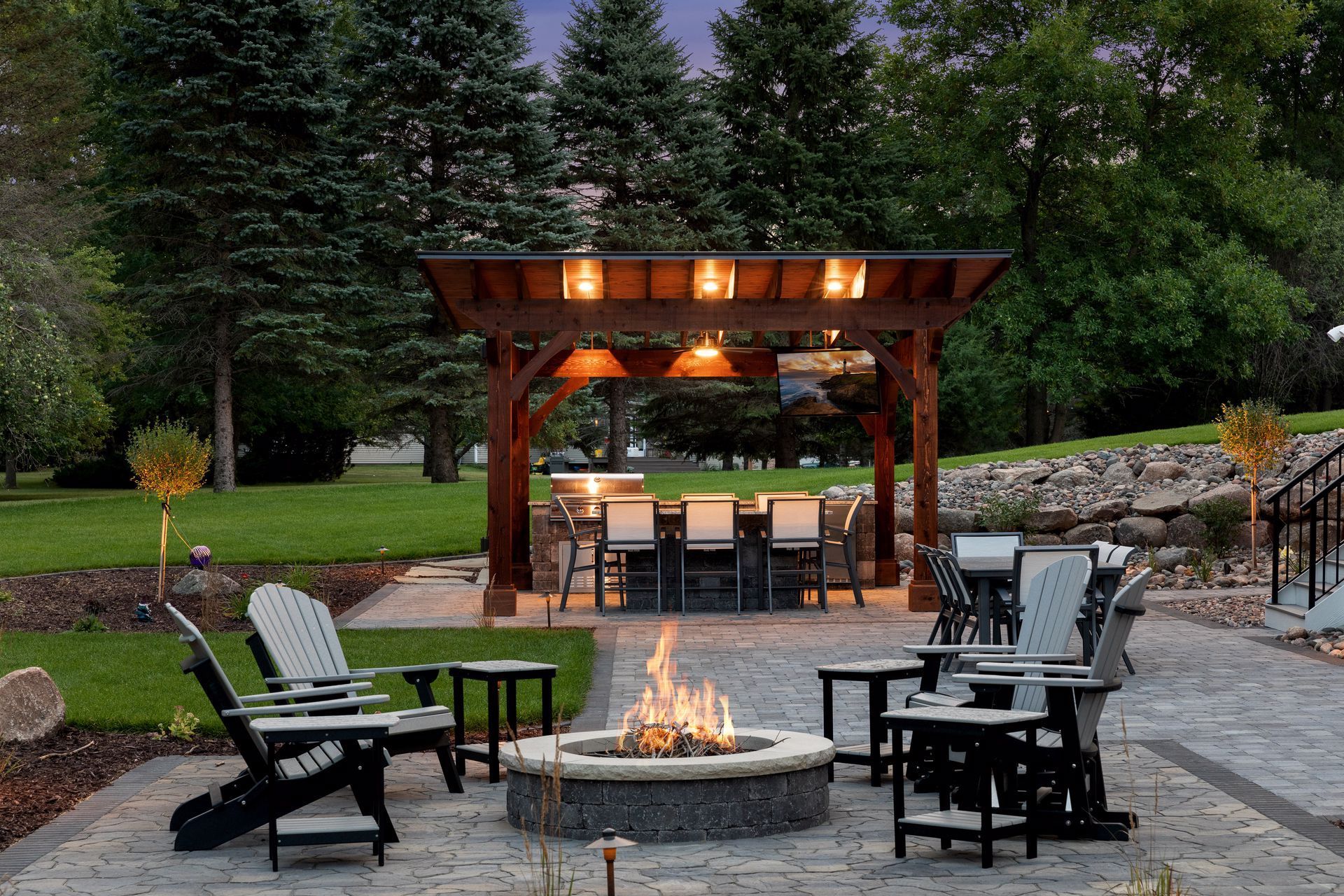 A fire pit is surrounded by chairs and tables under a pergola.