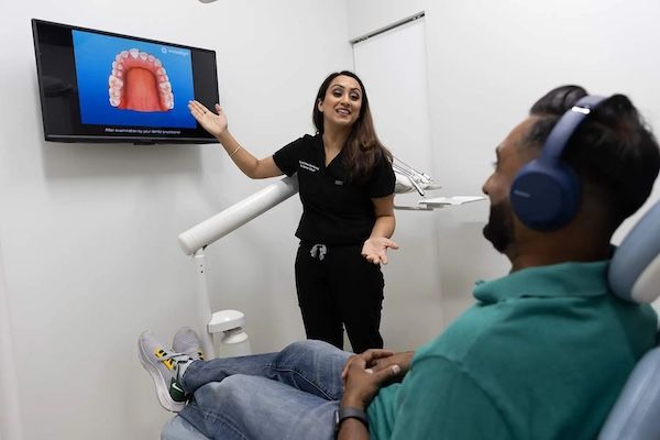 Dentist explaining dental procedure to patient in a clinic; woman pointing at screen showing teeth model.