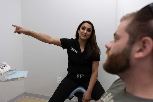 Woman in black scrubs points at something; man in chair looks at her in a dental office.