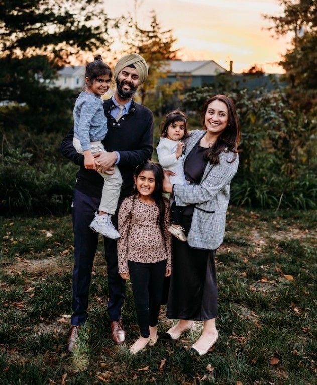 Family of five smiling outside. Man holds child, woman holds child, another child stands.