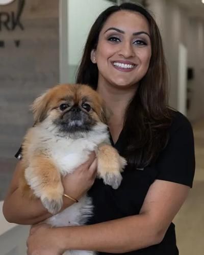 Woman in black scrubs smiles, holding a fluffy tan and white dog.