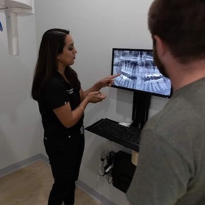 Dentist pointing at x-ray on monitor while explaining to a patient in a dental office.