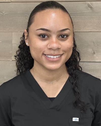 Young woman with dark hair and a small nose ring, smiling in a black scrub top.