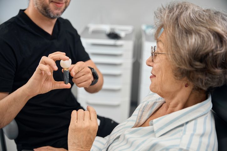 Dentist showing a patient a dental implant model in a dental office.