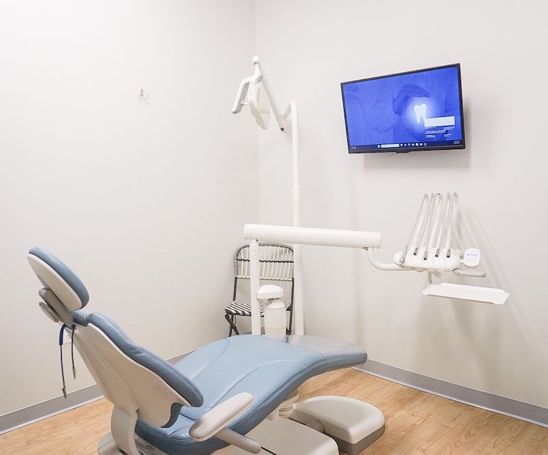 Dental chair in a white exam room with a mounted monitor, equipment, and light.