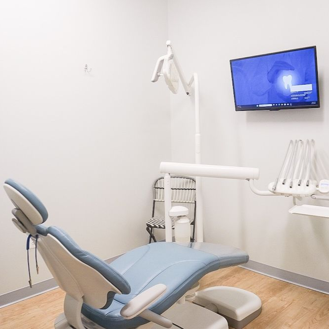 Dentist in black scrubs consults with a male patient in khaki pants and a green shirt in a dental office.