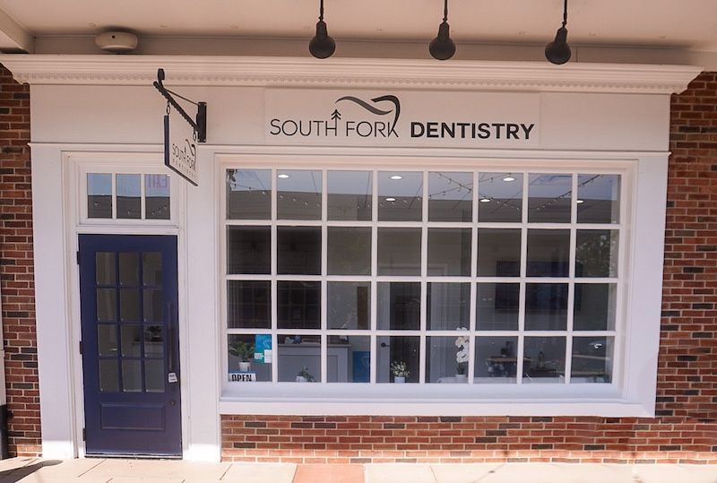 South Fork Dentistry storefront with a blue door and large, white-framed window. Red brick exterior.