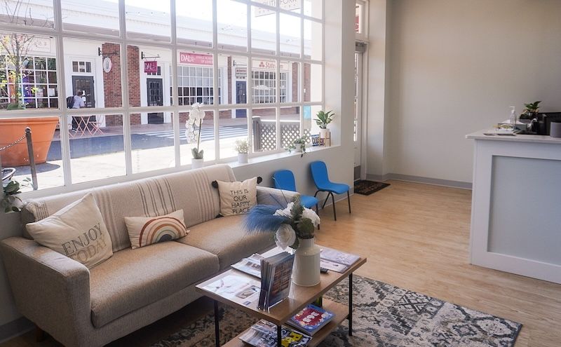 Lobby with sofa, coffee table, and large window overlooking an outdoor area with storefronts.