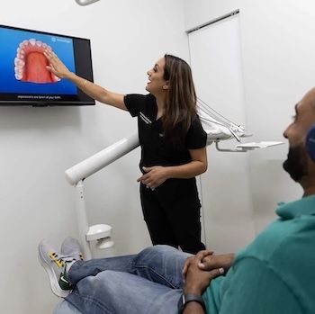 Dentist explaining dental procedure to patient in a dental office, pointing to screen with a digital teeth model.