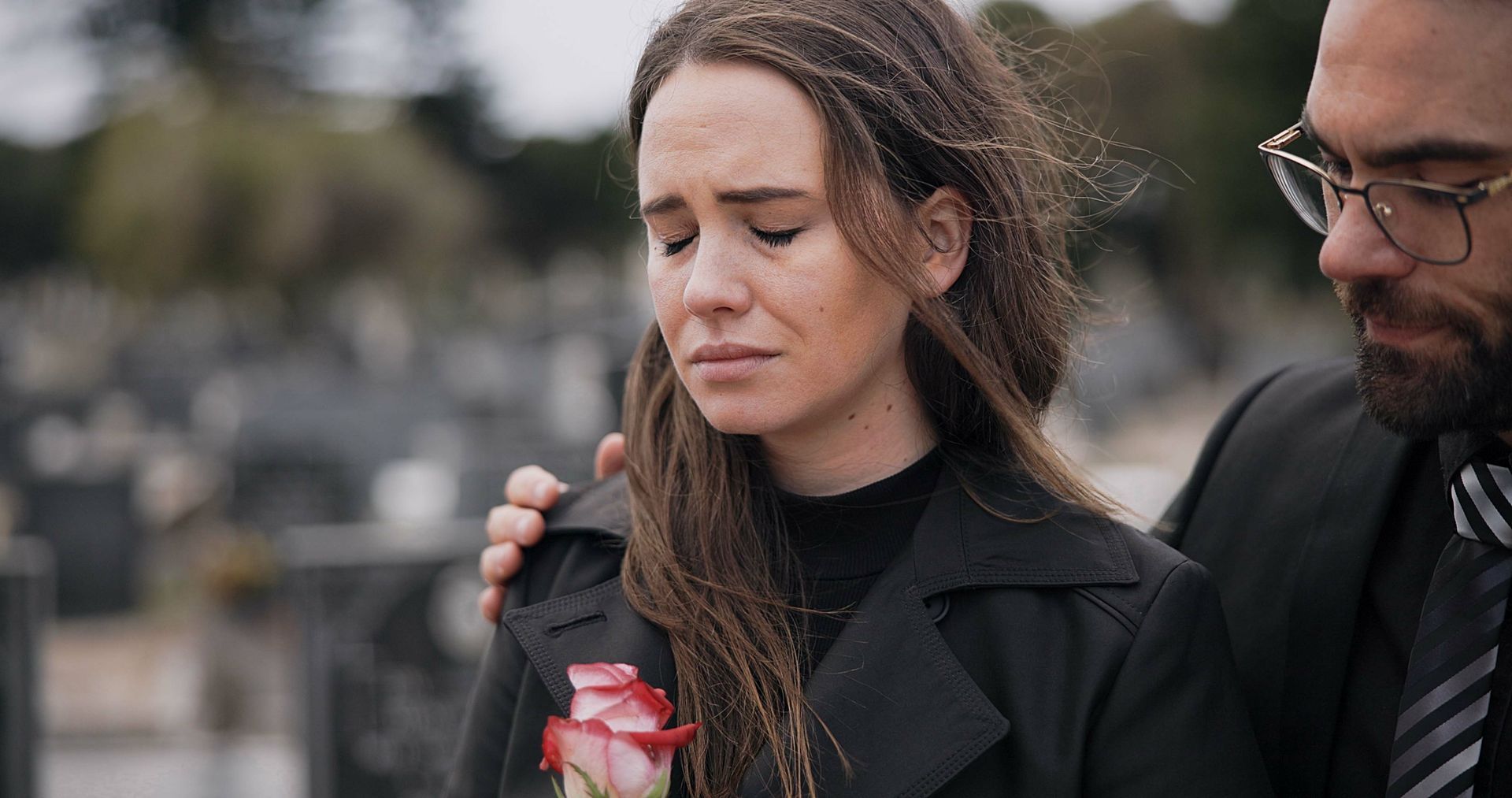 A man is comforting a woman who is crying in a cemetery.