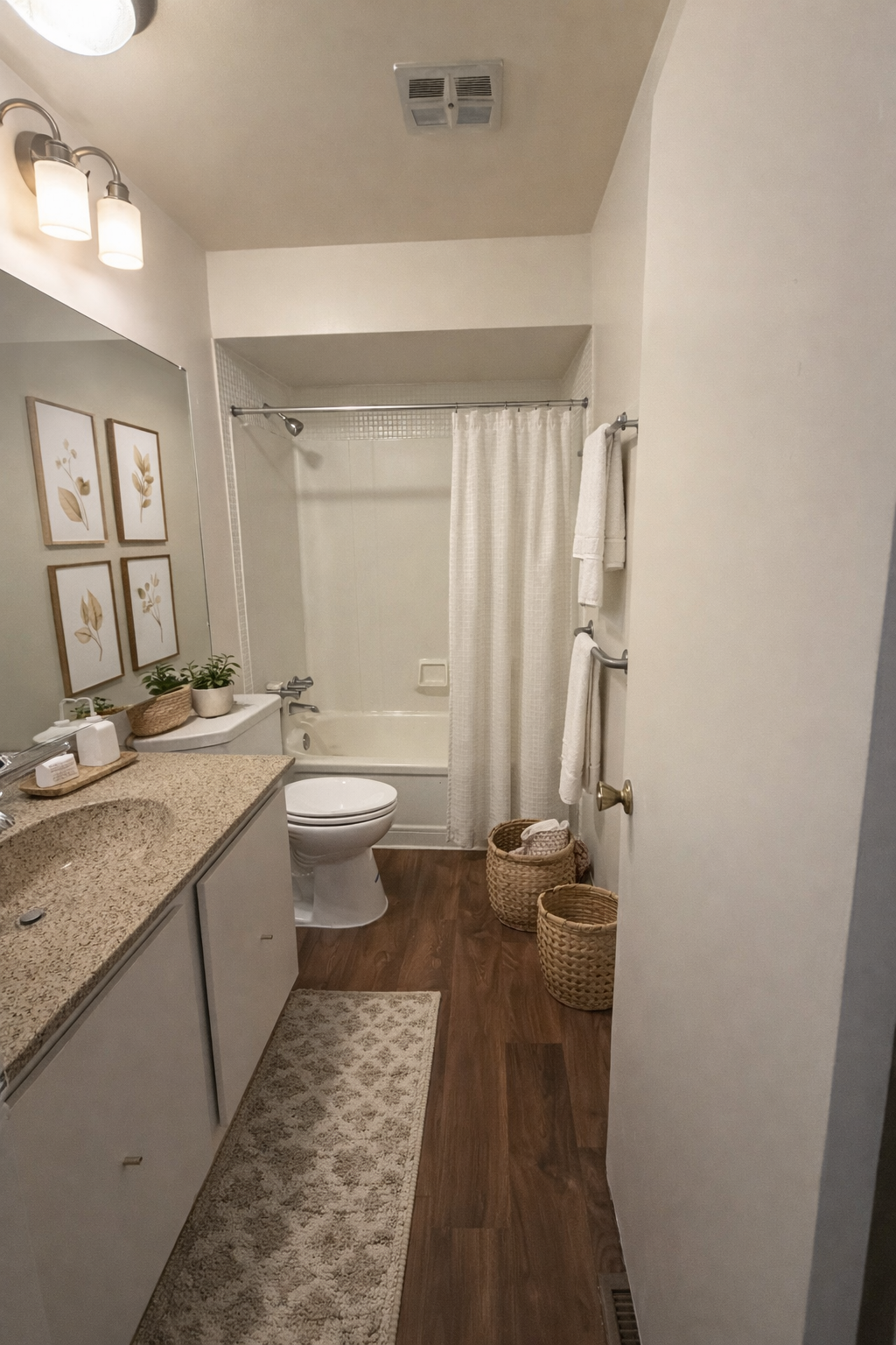 Bathroom with a vanity, toilet, and bathtub/shower. Neutral color scheme, wood-look floor, and decorative baskets.