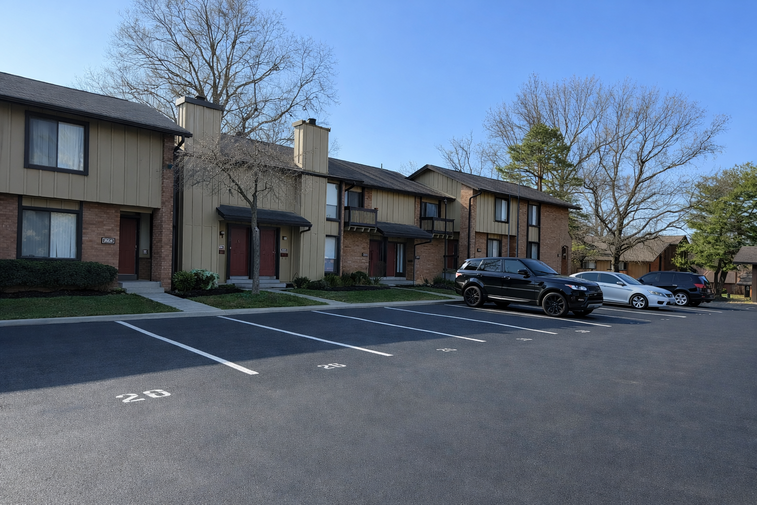 Townhouses with assigned parking spots. Cars parked in front of the buildings. Blue sky, bare trees.