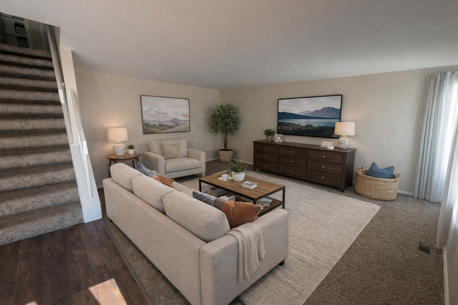 Spacious living room with a couch, armchair, TV, rug, and staircase. Neutral colors and natural light.
