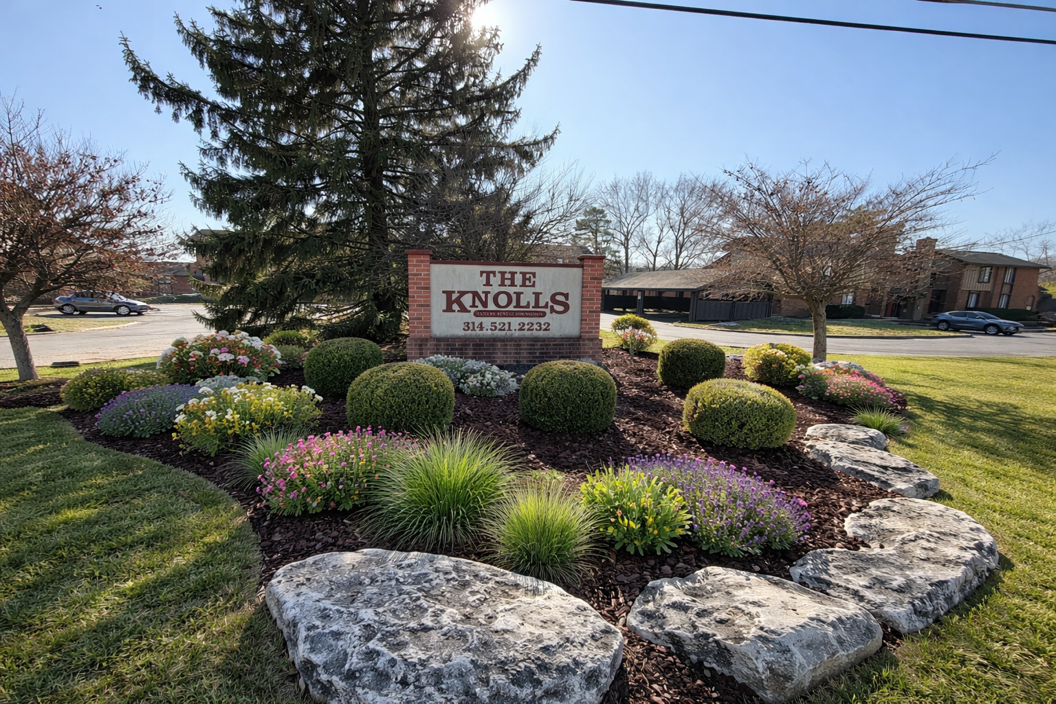 Sign for The Knolls apartment complex, surrounded by landscaped flowers, bushes, and large rocks.