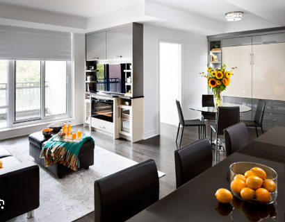 Modern open-plan living room and dining area with gray and black furniture, large windows, and flowers on the table